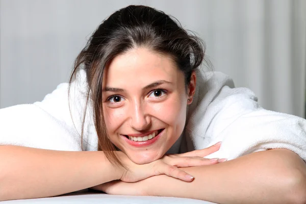 Młoda kobieta uśmiechający się w szlafrok, leżąc na brzuchu — Zdjęcie stockowe