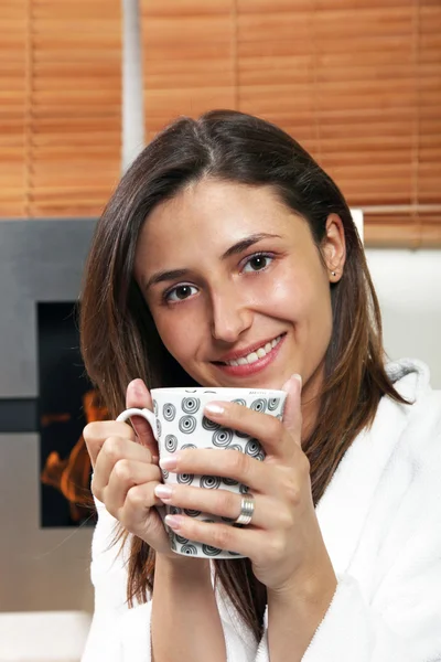 Mladá žena s čaj nebo kávu u krbu — Stock fotografie