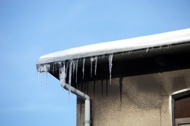 Dangerous icicles on the house against a blue sky - space for text clipart