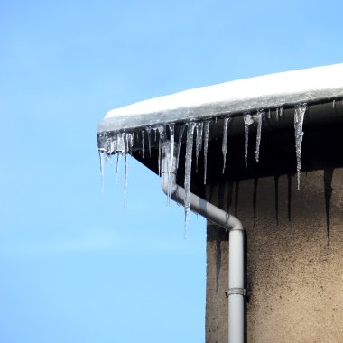 Danger - small icicles hanging from the gutter in front of blue sky clipart