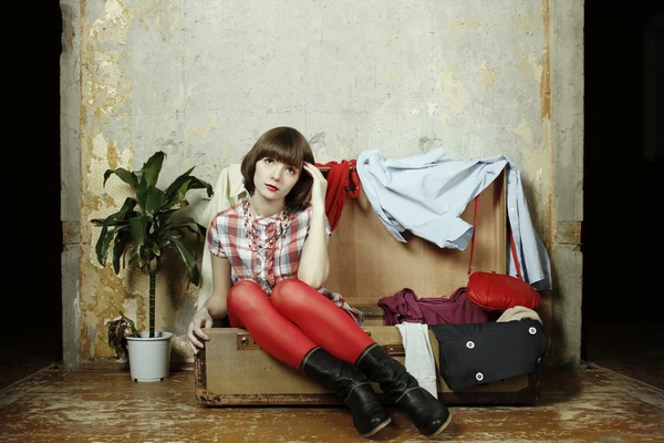 Молодая женщина сидит в чемодане, наполненном одеждой — стоковое фото