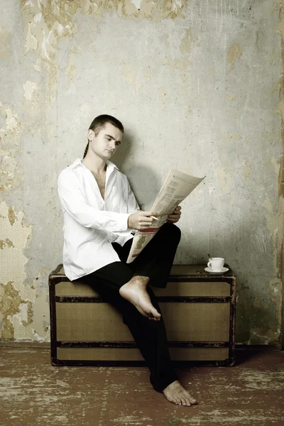 Мужчина сидит на чемодане и читает газету — стоковое фото