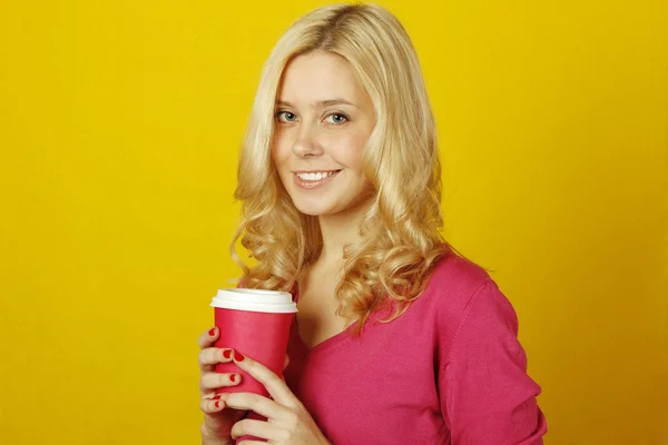 コーヒーの紙コップを保持している黄色の背景に美しい若い女性 — ストック写真