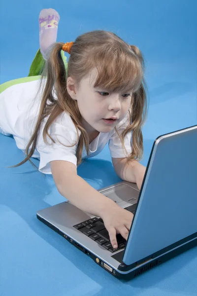 Den lilla flickan använder dator på blå Royaltyfria Stockfoton