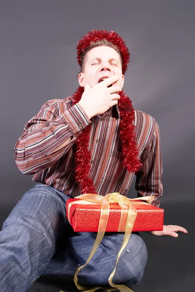 A man yawns, laying a gift on knees — Stock Photo, Image