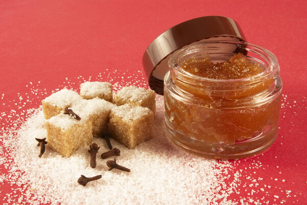 Скраб для тела с коричневыми кристаллами сахара, пряностями, на красном фоне
