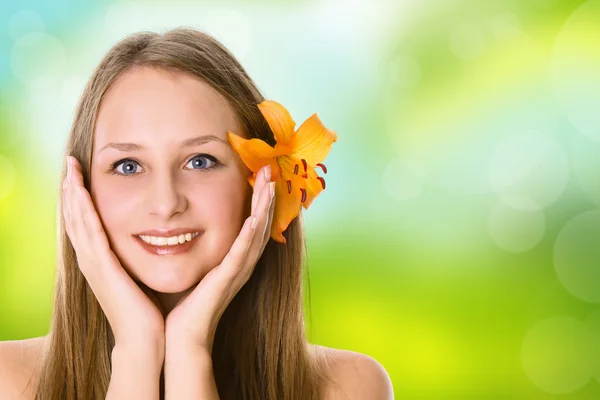 Mooie vrouw gezicht met een bloem op groene onscherpe achtergrond — Stockfoto
