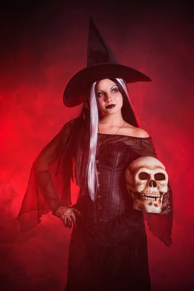 Halloween-Hexe mit Totenkopf über farbigem Hintergrund mit Rauch — Stockfoto