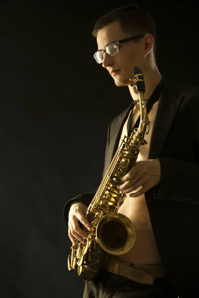 The young jazzman with a saxophone on black — Stock Photo, Image