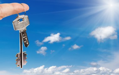 Finger with key against blue sky background clipart