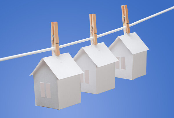 Paper houses with clothespins, hanging from rope on blue background. Real estate concept