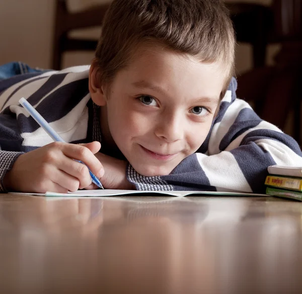 Pojke gör lektioner som ligger på golvet — Stockfoto