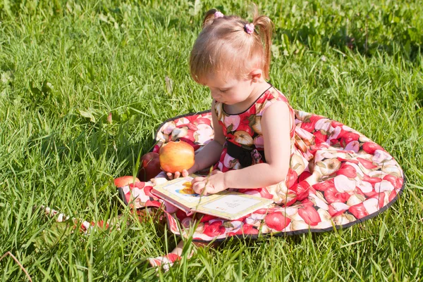 Meisje eten een appel en op zoek boek op het gras — Stockfoto