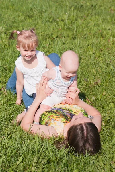 Mamma liggande på gräset två barn på hennes mage, spela — Stockfoto