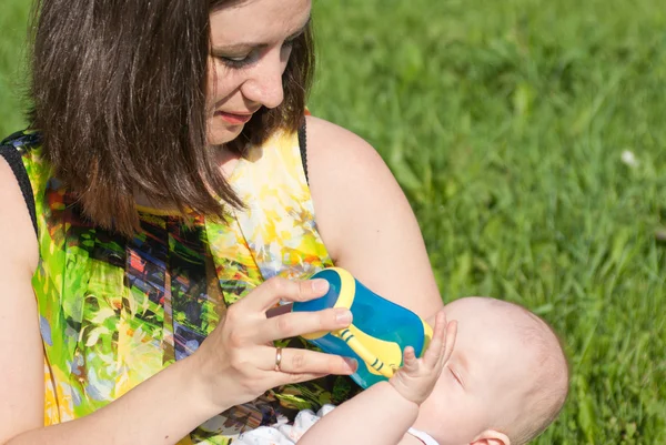 Mom waters the baby bottle in the park — Stock Photo, Image