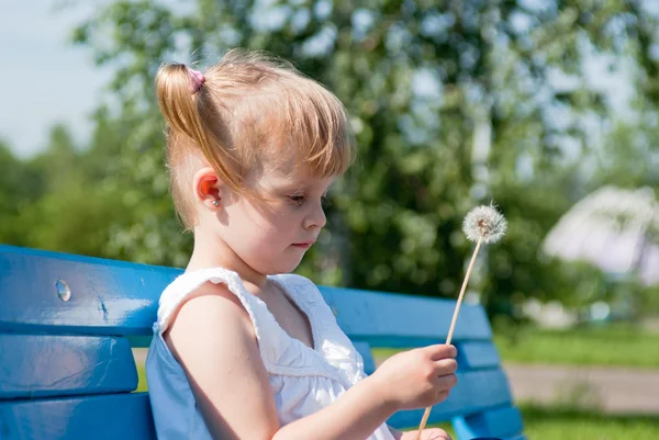 Задумчивая девушка с одуванчиком на скамейке в парке — стоковое фото