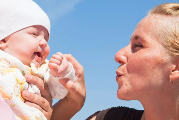 Mom kisses a happy child, against the sky — Stock Photo, Image