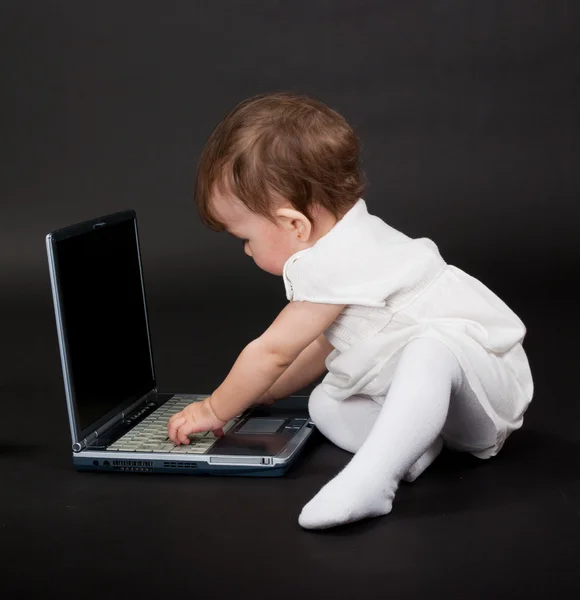 在笔记本电脑上黑色背景白色连衣裙的小女孩 — 图库照片