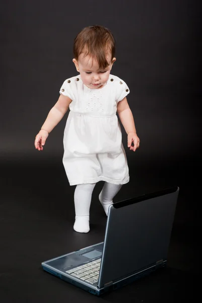 在笔记本电脑上黑色背景白色连衣裙的小女孩 — 图库照片