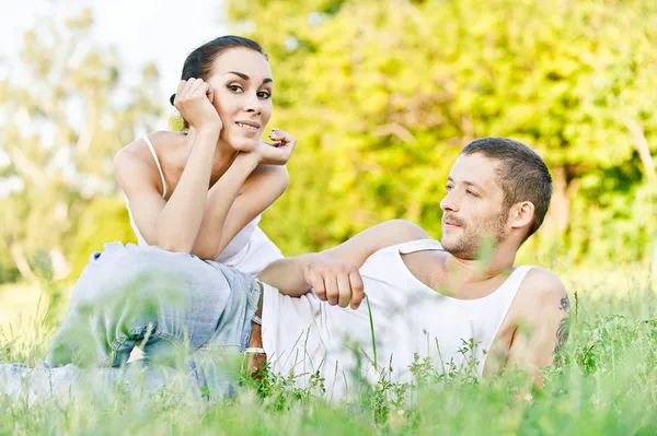 Jovem casal bonito senta-se na grama — Fotografia de Stock