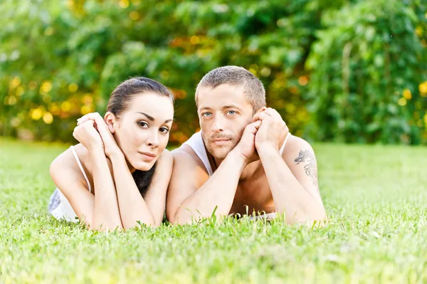 Jovem casal bonito senta-se na grama — Fotografia de Stock