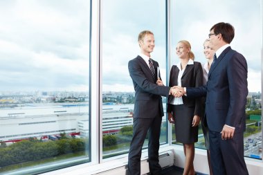 Two businessmen shake hands next to business women clipart