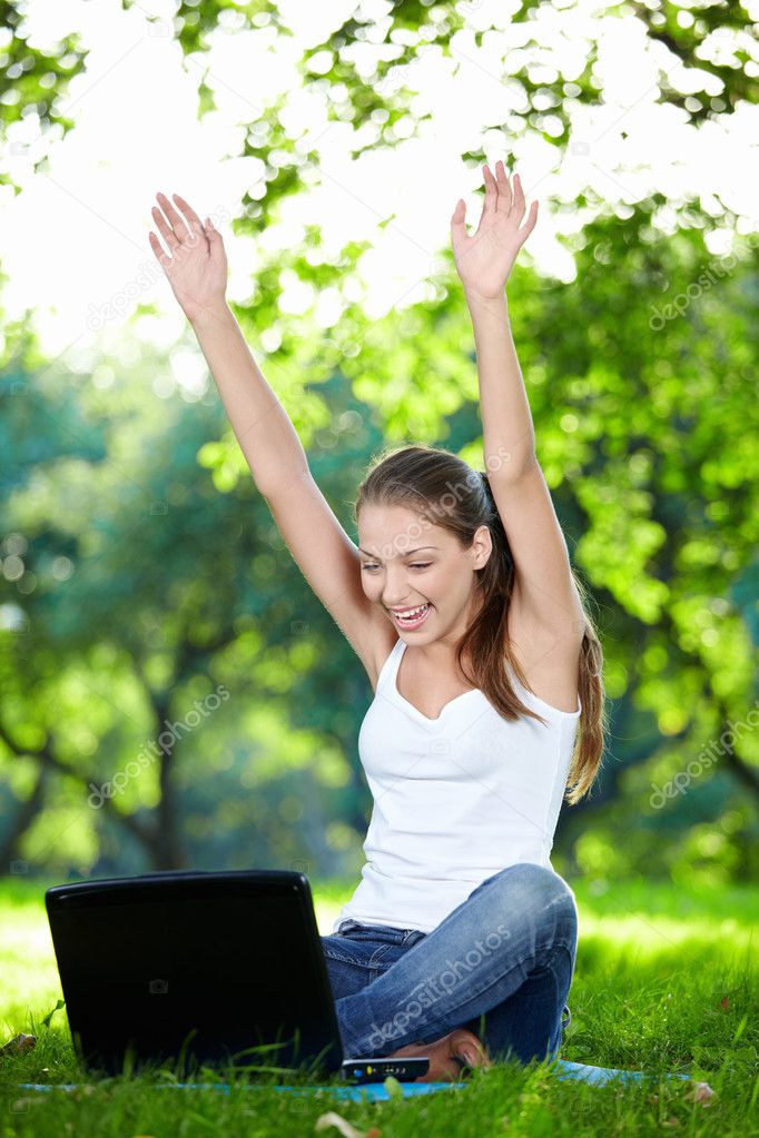 A smiling girl with his hands up a laptop in the park