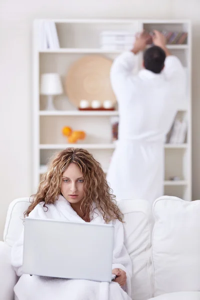 一个女孩在看着一台笔记本电脑在前景浴袍 — 图库照片