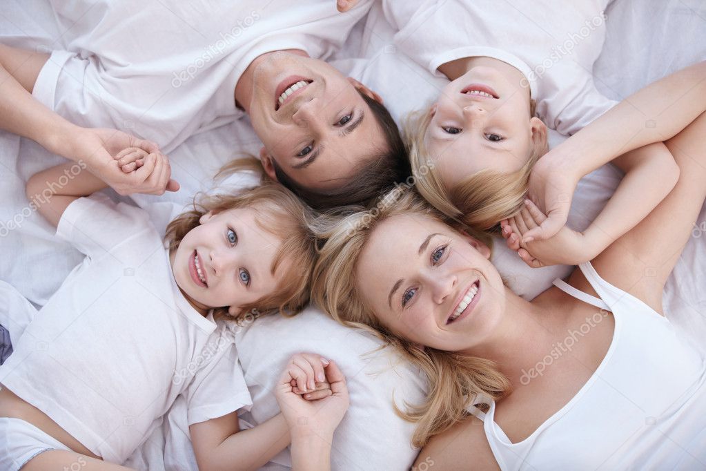 Smiling family lie on a white bed