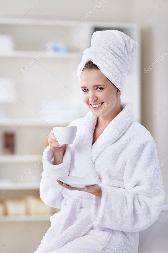 A beautiful young girl in a bathrobe and a towel with a cup of coffee