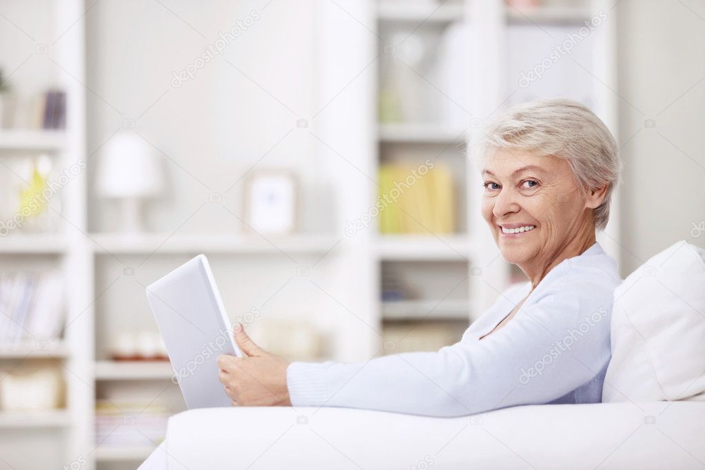 Smiling elderly woman on the couch with a laptop