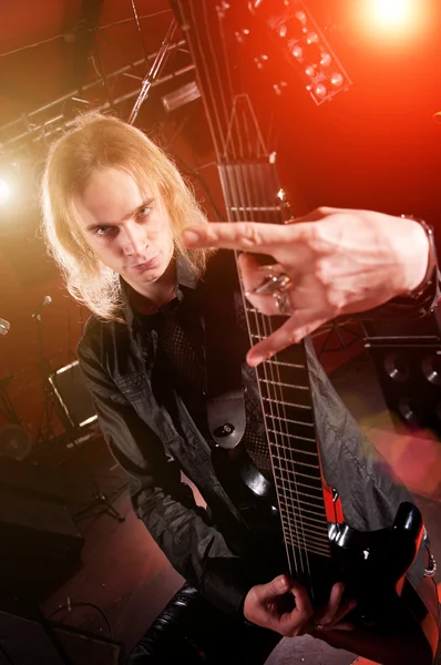 Длинноволосый гитарист играет и делает рок-руку — стоковое фото