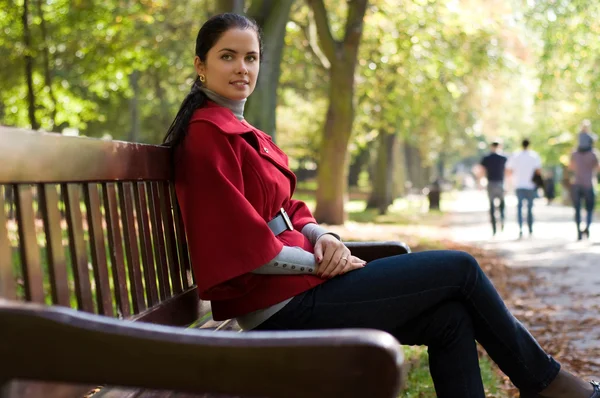 Jovem caucasiana sentada em um parque em um banco de madeira , — Fotografia de Stock