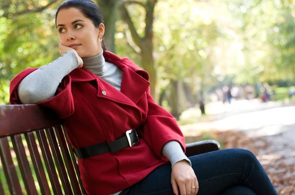Νεαρή καυκάσιος γυναίκα που κάθεται σε ένα πάρκο σε ένα ξύλινο παγκάκι, — Φωτογραφία Αρχείου