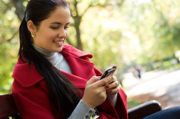 Joven mujer caucásica con un teléfono celular, sentada en un parque — Foto de Stock