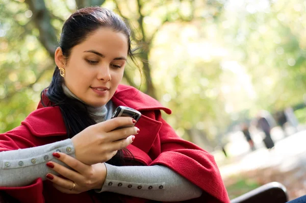 Fiatal kaukázusi nő egy mobiltelefon, egy park ül — Stock Fotó