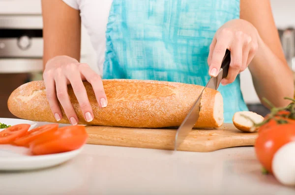 Женщина режет хлеб на кухне (мелкий DOF ) — стоковое фото