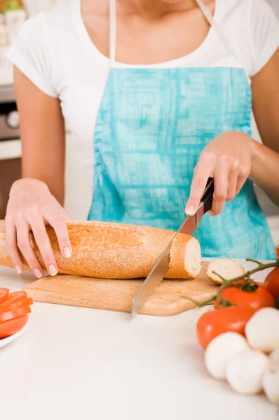 Mujer cortando pan en la cocina — Foto de Stock