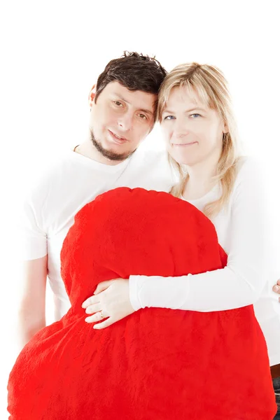 Pareja feliz sosteniendo almohada roja sobre blanco — Foto de Stock