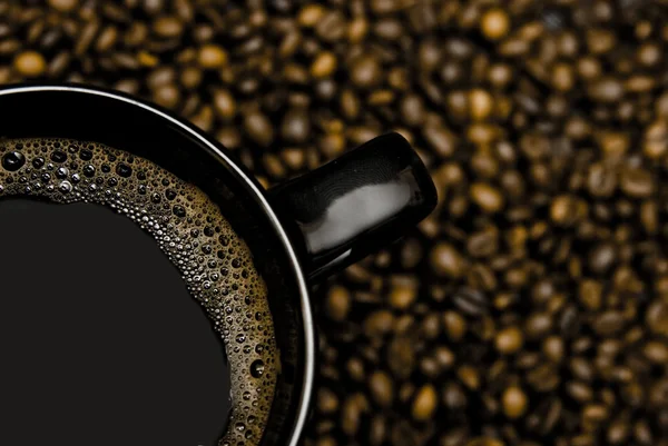 Black mug of coffee and scattered beans — Stock Photo, Image