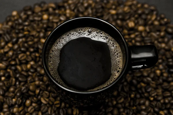 Black mug of coffee and scattered beans — Stock Photo, Image