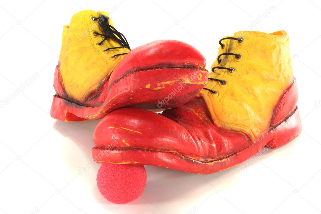 Red and yellow clown shoes stand on a red clown nose