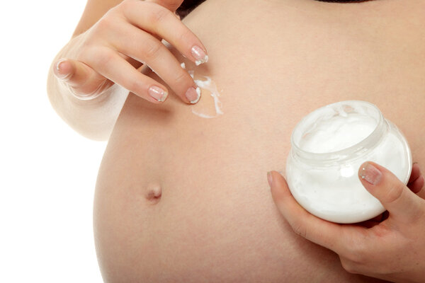 Young pregnant woman rubs cream into her belly