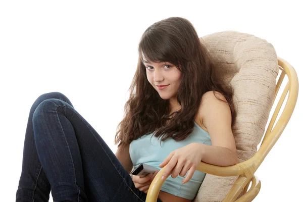 坐在扶手椅上视图从电视上和远程控制看电视的青少年女子 — 图库照片