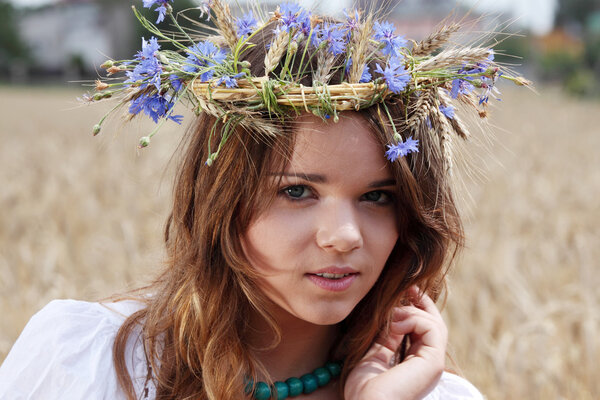 Beautiful young girl in summer field with grain and flower garland