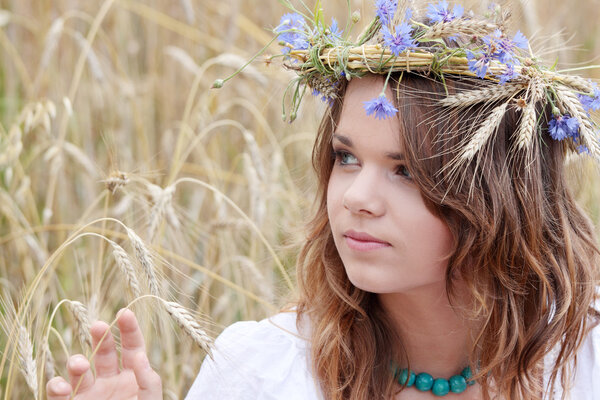Beautiful young girl in summer field with grain and flower garland