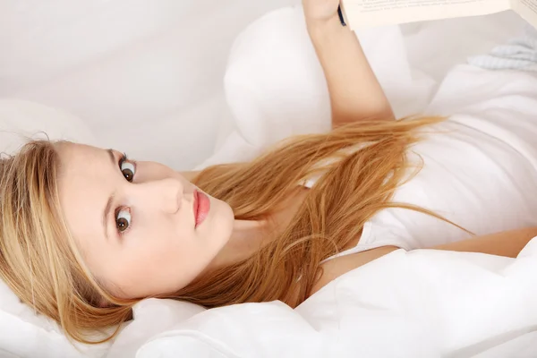 Молодая блондинка читает книгу на кровати — стоковое фото