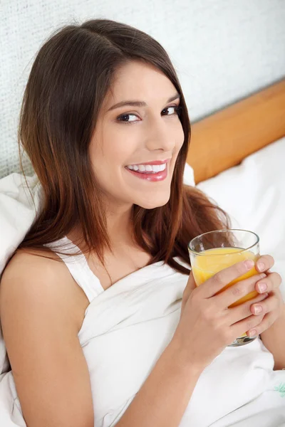 Mulher na cama bebendo suco de laranja — Fotografia de Stock