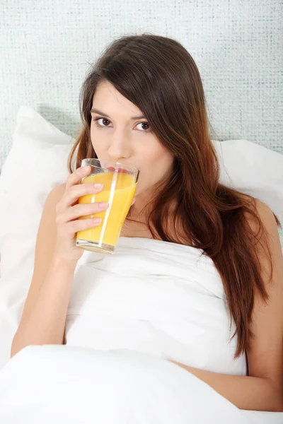 Γυναίκα στο κρεβάτι πίνοντας χυμό πορτοκαλιού — Φωτογραφία Αρχείου