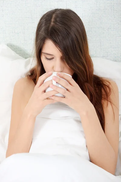 坐在她的床上在早上喝一杯咖啡的可爱女人 — 图库照片